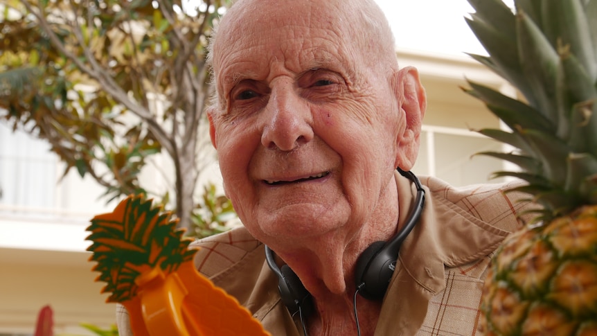 older man smiling next to a pineapple.