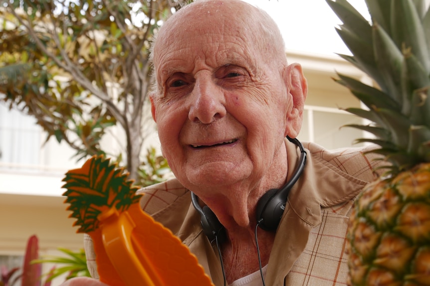 older man smiling next to a pineapple.