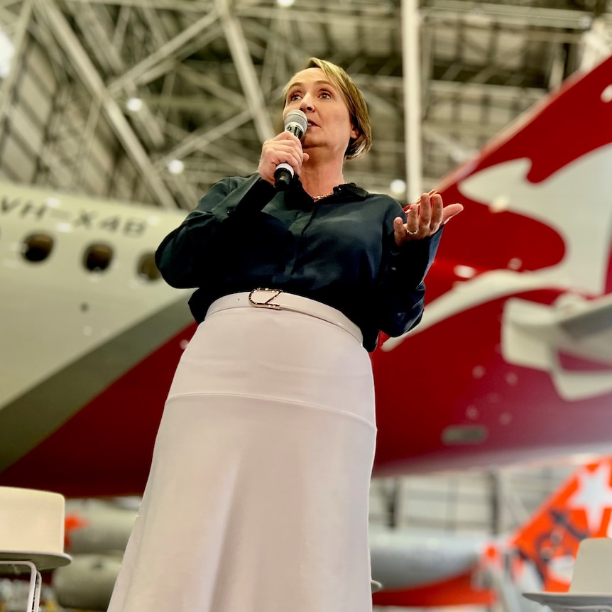 Qantas CEO Vanessa Hudson stands in front of Qantas and Jetstar planes in a hanger, with both airlines' logos visible.