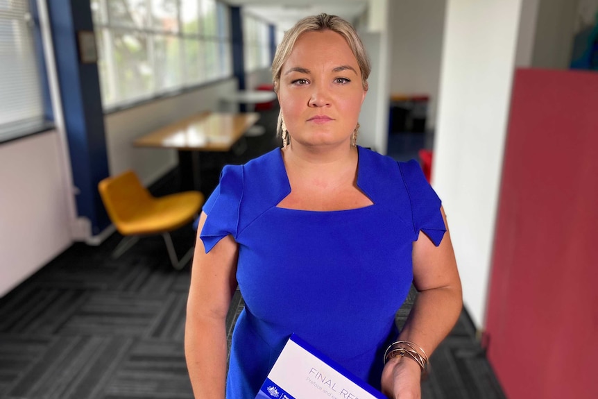 Clare Leaney wearing a blue dress and holding a report.