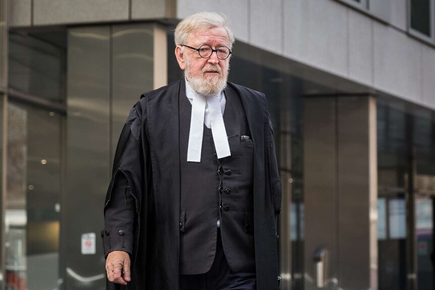 Dressed in courtroom attire, Robert Richter QC walks outside a court building.