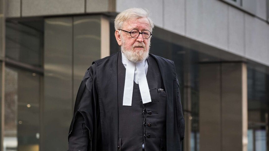 Dressed in courtroom attire, Robert Richter QC walks outside a court building.