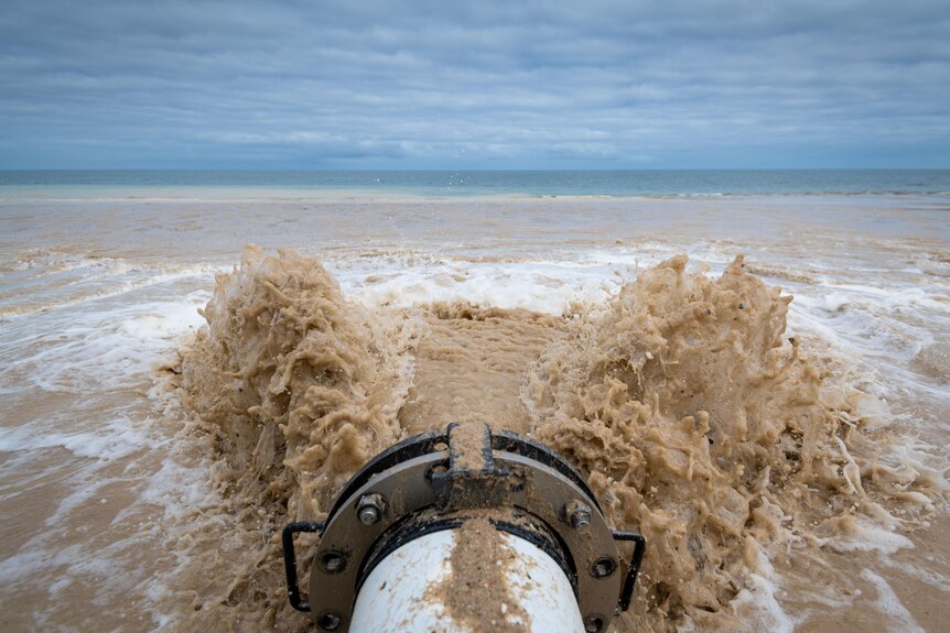 A torrent of water and sand at the mouth of a pipe on an Adelaide beach.