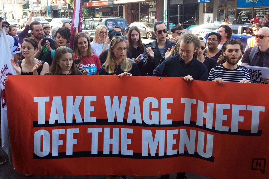 Workers and union members hold up an orange banner that says 'Take wage theft off the menu."