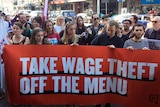 Workers and union members hold up an orange banner that says "Take wage theft off the menu."
