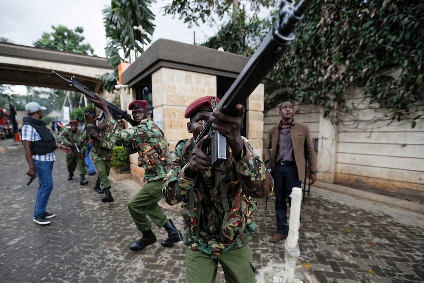 Kenyan security forces aim their weapons up at buildings as they run through a hotel complex.