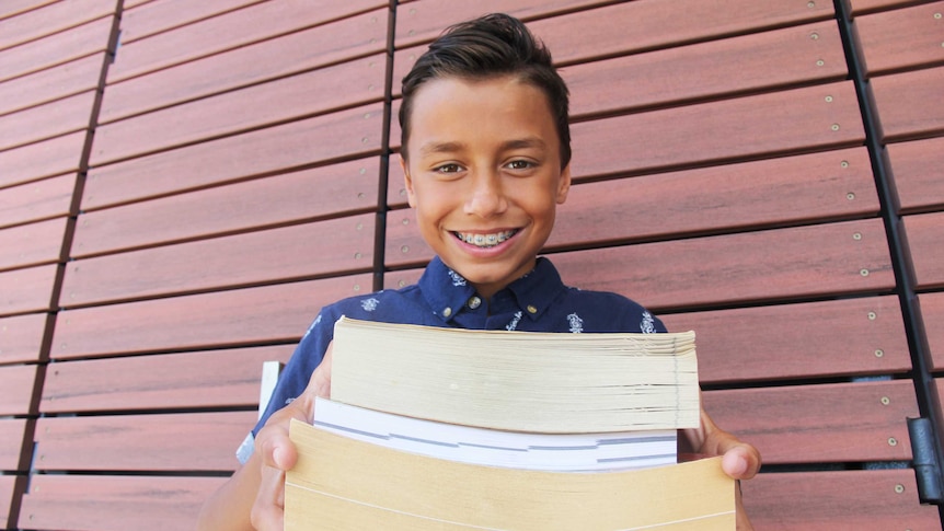 A boy smiles holding out a stack of books