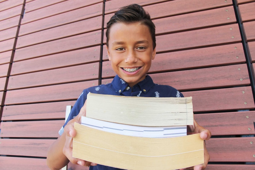 A boy smiles holding out a stack of books