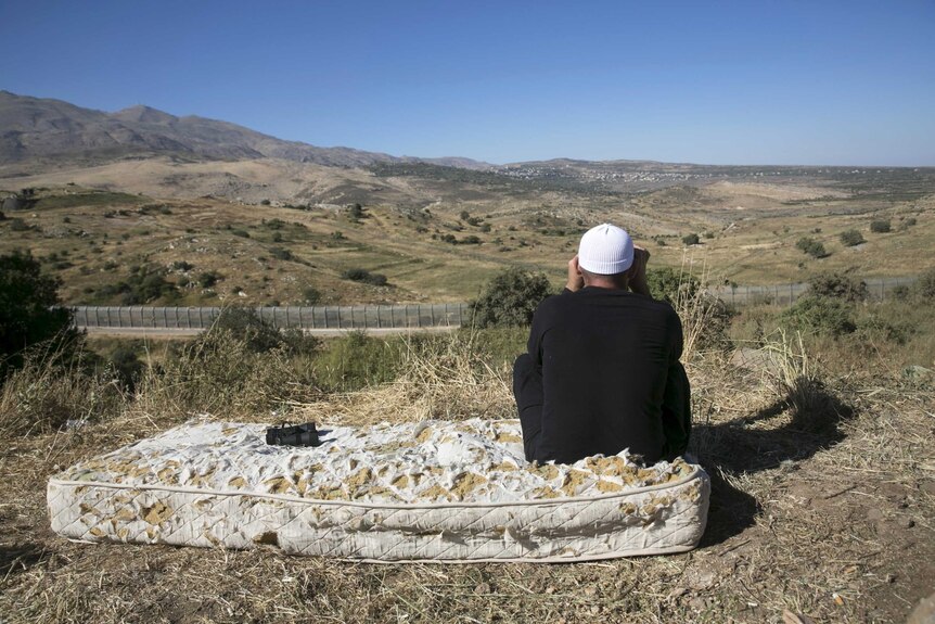 A member of the Druze community uses binoculars to watch the fighting in Syria