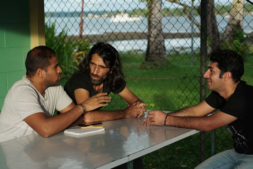 Three men sitting at a table near a beach