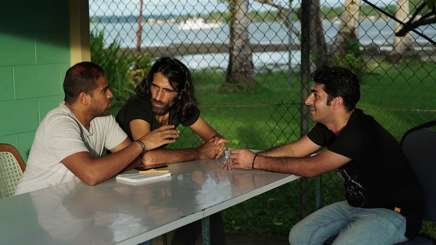 Three men sitting at a table near a beach