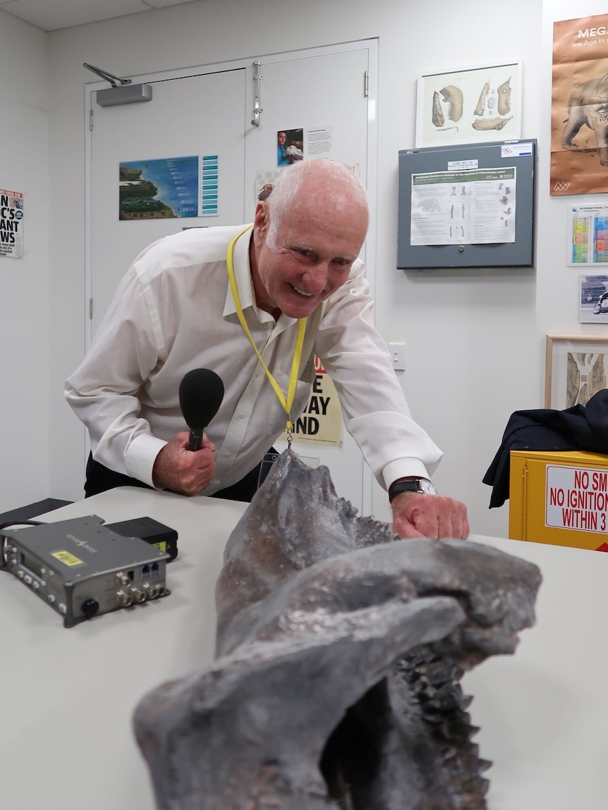 Man with microphone looking at dinosaur bone.