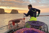 A man with lobster nets on a boat with colourful dawn sky.