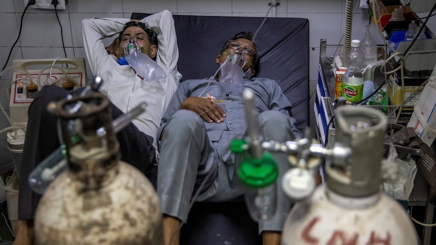 Two COVID-19 patients share a hospital bed as they are given oxygen.