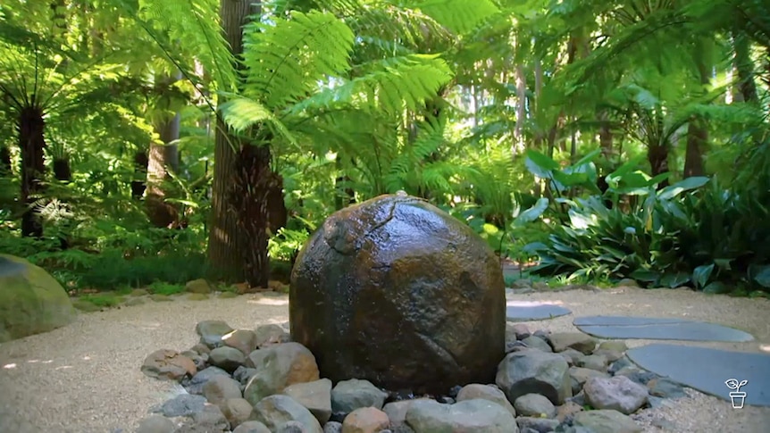 Large rock fountain in the middle of a green-canopied garden.