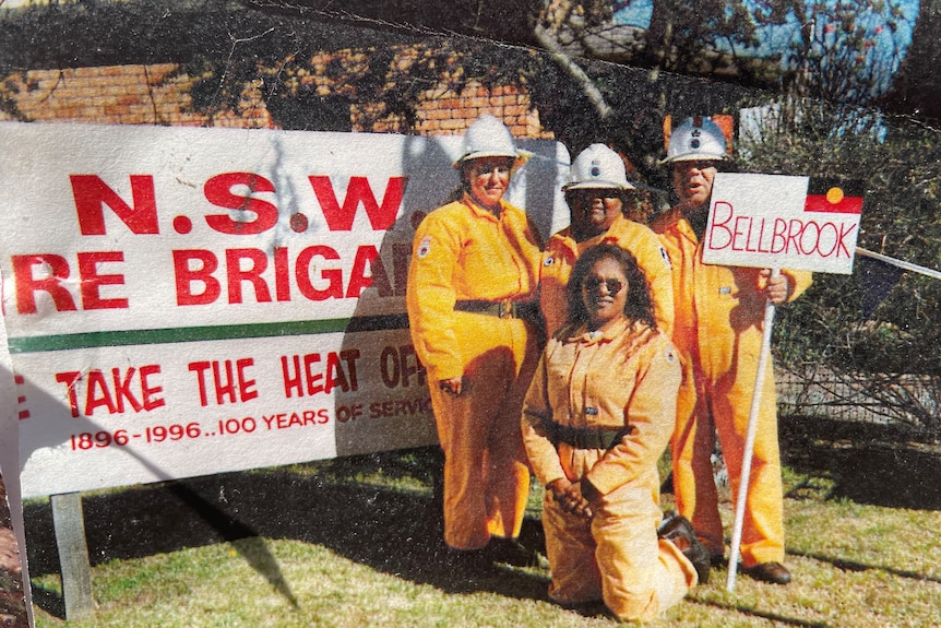 An Aboriginal fire crew holding a sign saying 'Bellbrook' with the Aboriginal flag on the sign.
