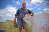 Townsville man Dave Dudley holds a piece of plastic waste, he stands in front of illegal dumping signs erected in a paddock.