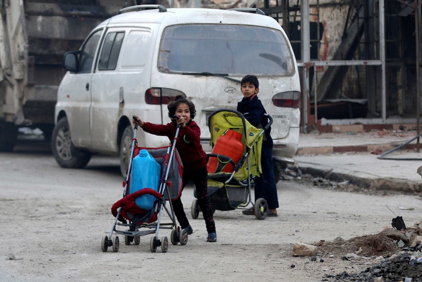 Children push containers in strollers in a run-down part of Aleppo, Syria.