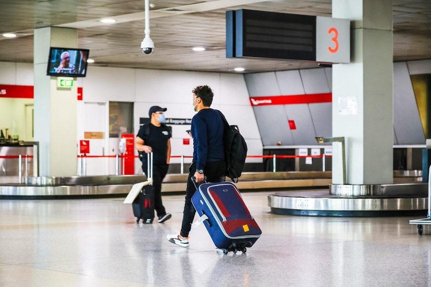 Deux passagers masculins roulant des valises dans un terminal d'aéroport.