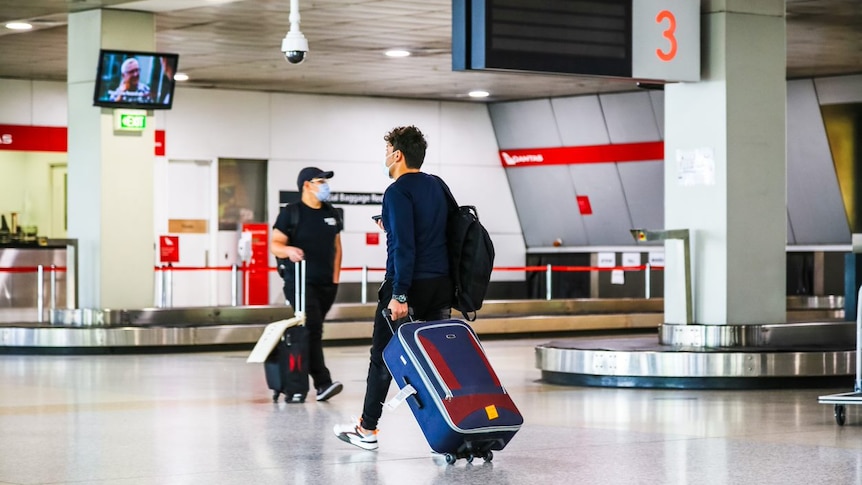 Two male passengers wheeling suitcases in an airport terminal.