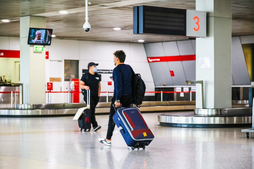 Two male passengers wheeling suitcases in an airport terminal.