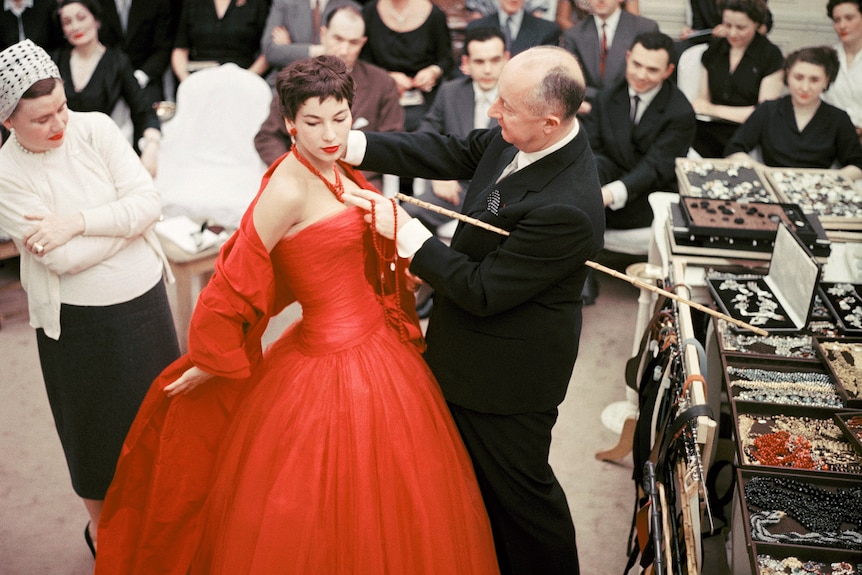 Christian Dior adjusts accessories on a model's dress in 1954.