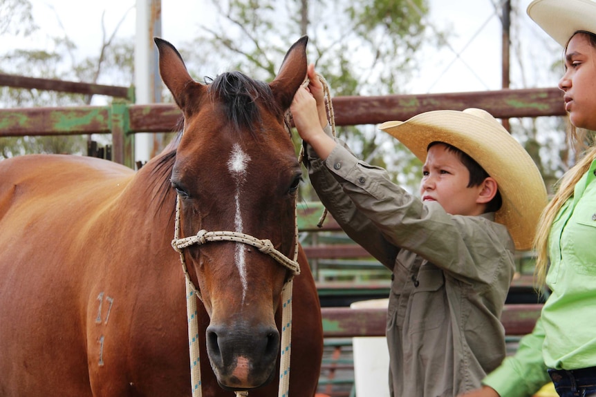 A boy ties a knot on a horse halter.