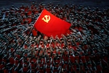 A huge crowd of performers hold their hands towards a large Chinese flag