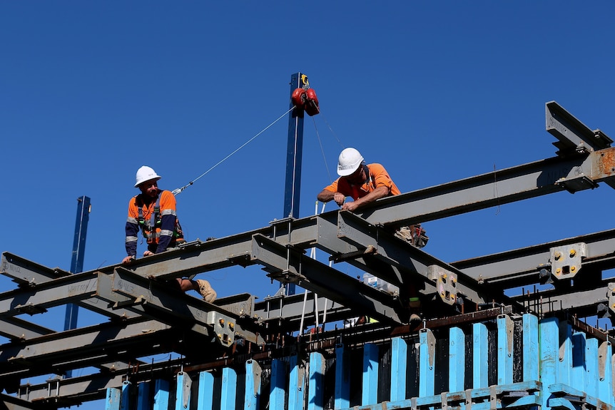 Two construction workers work on steel beams with the blue sky behind them