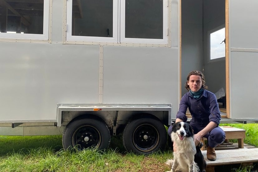 A person and a dog sitting in front of a tiny house