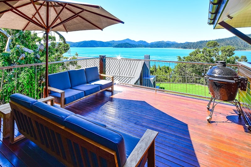 A wooden deck with outdoor lounge setting overlooking grassed area and crystal blue water.