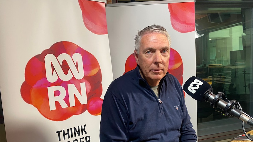 A man with silver hair, wearing a blue shirt, sitting in front of a microphone, with the Radio National logo in the background.