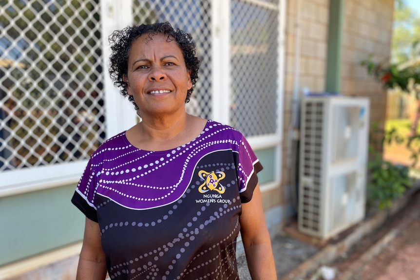A woman wearing an Indigenous design purple-and-black top stands outside an office.