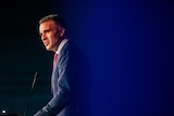 A man in a suit speaking on a podium