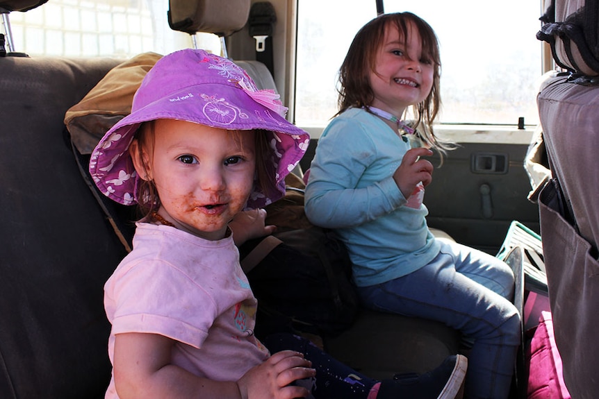 Young sisters, Madeline and Isabella, smile at the camera while sitting in the back seat of their father's ute.