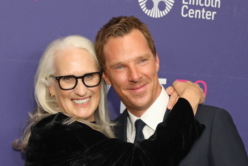 67-year-old white woman with long white hair and black-rimmed glasses hugging 45-year-old white man with blue eyes brown hair. 