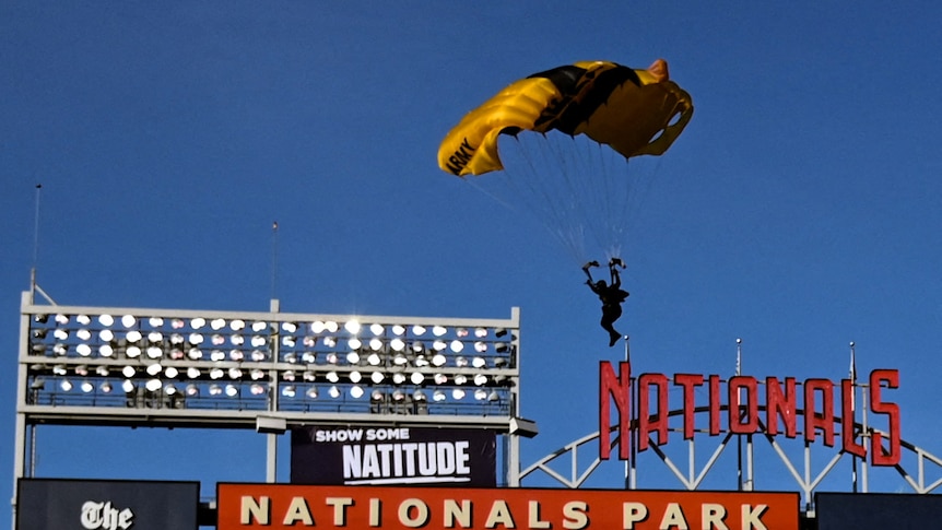 A person in a yellow parachute flies above a stadium.