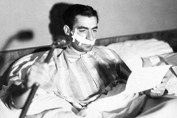 Man in striped pyjamas with a bandage on his face, reading a document.