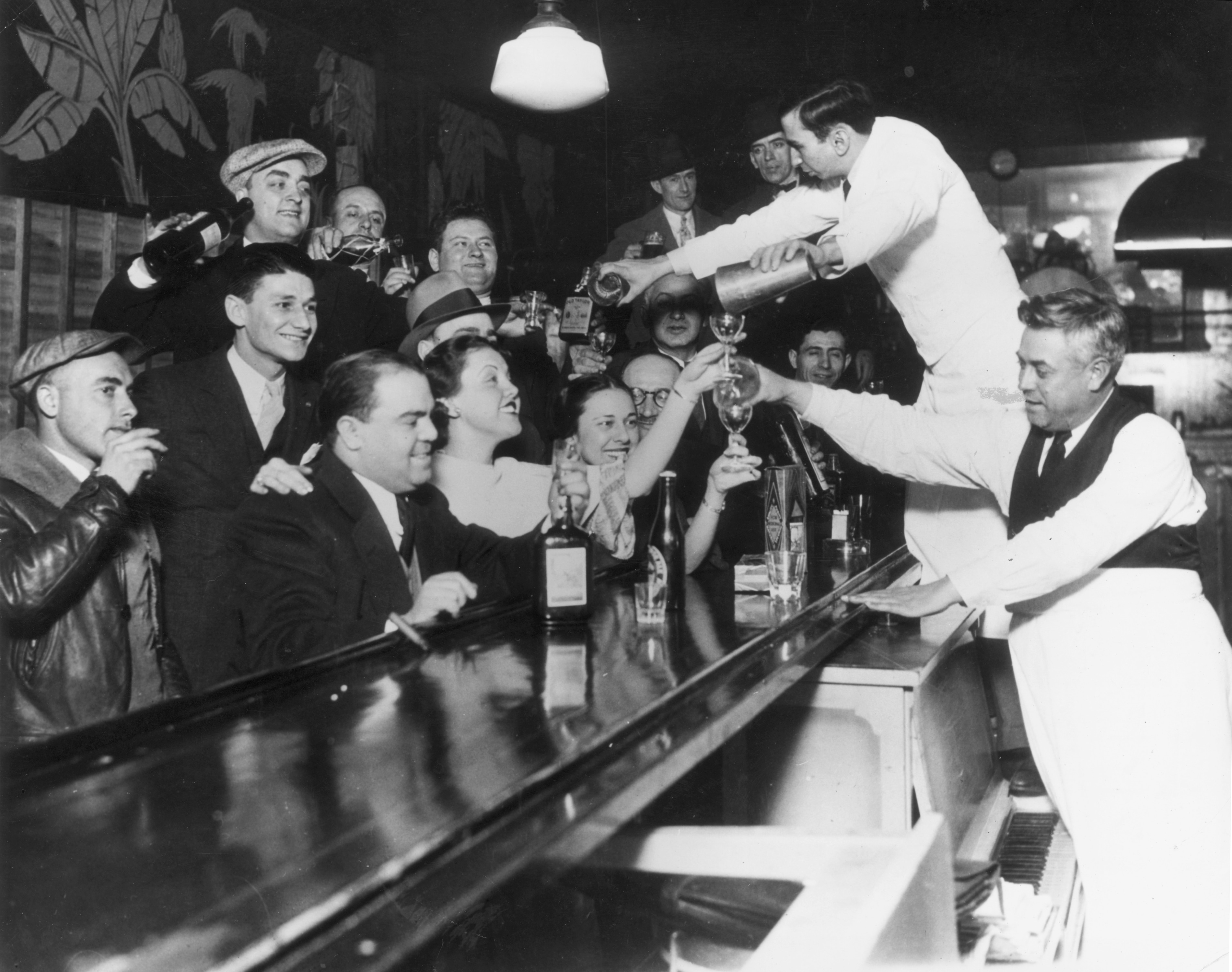 Bartenders pour a round of drinks for customers lined up around a counter.