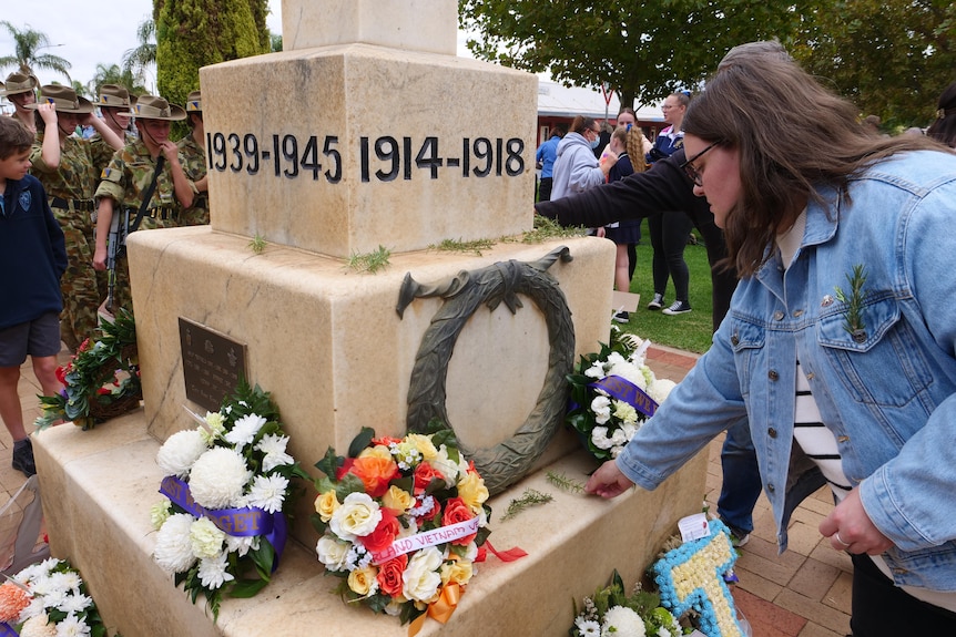 A woman places rosemary on a war memorial.