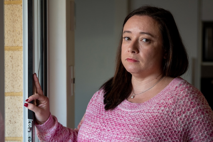 Woman with dark hair in pink top standing at doorway looking to camera