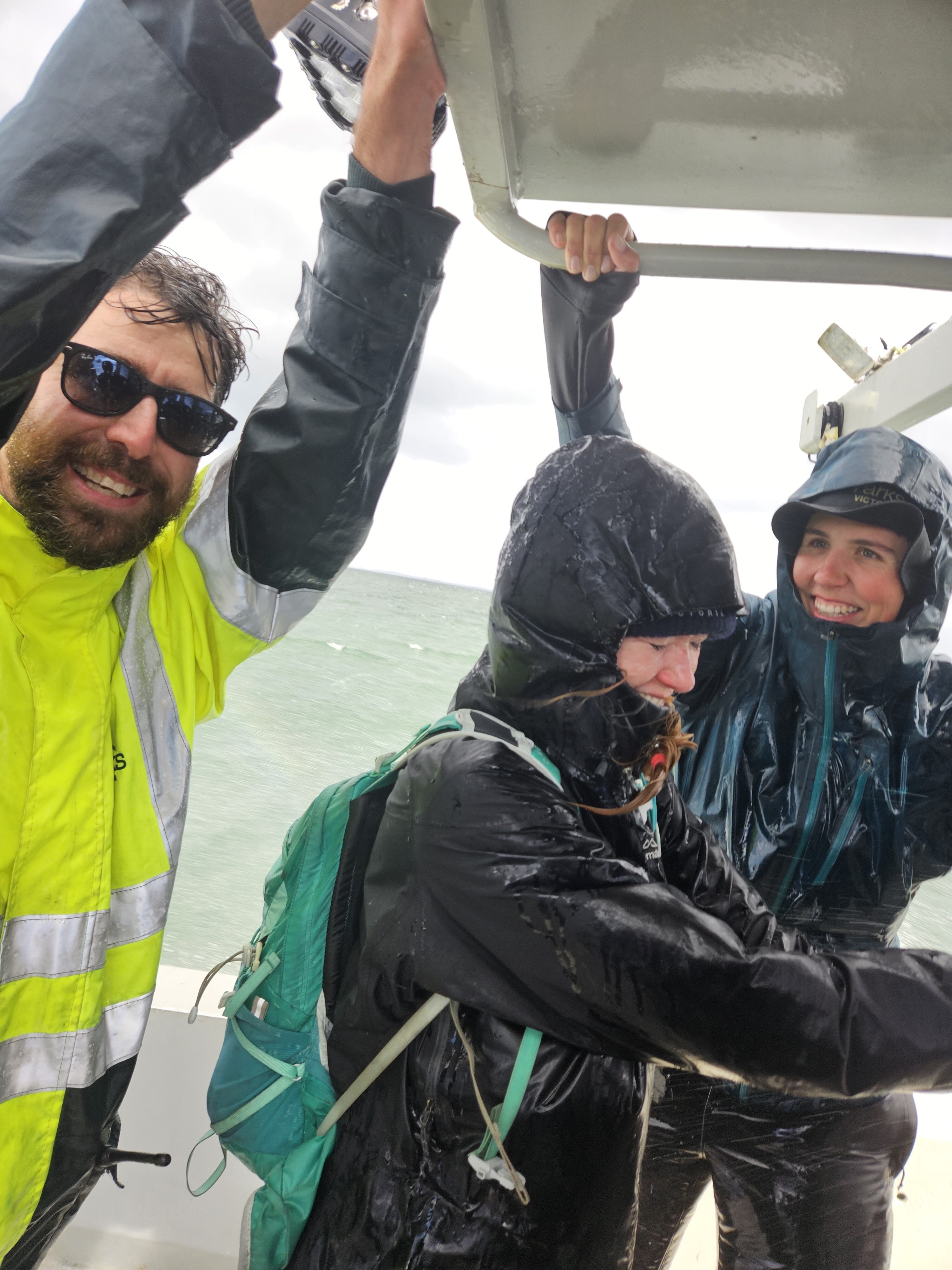 Parks rangers in hi-vis holding onto the boat in stormy conditions. 