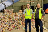 Two men stand in front of a pile of recyclable cans at the Cherbourg Material Recovery Centre