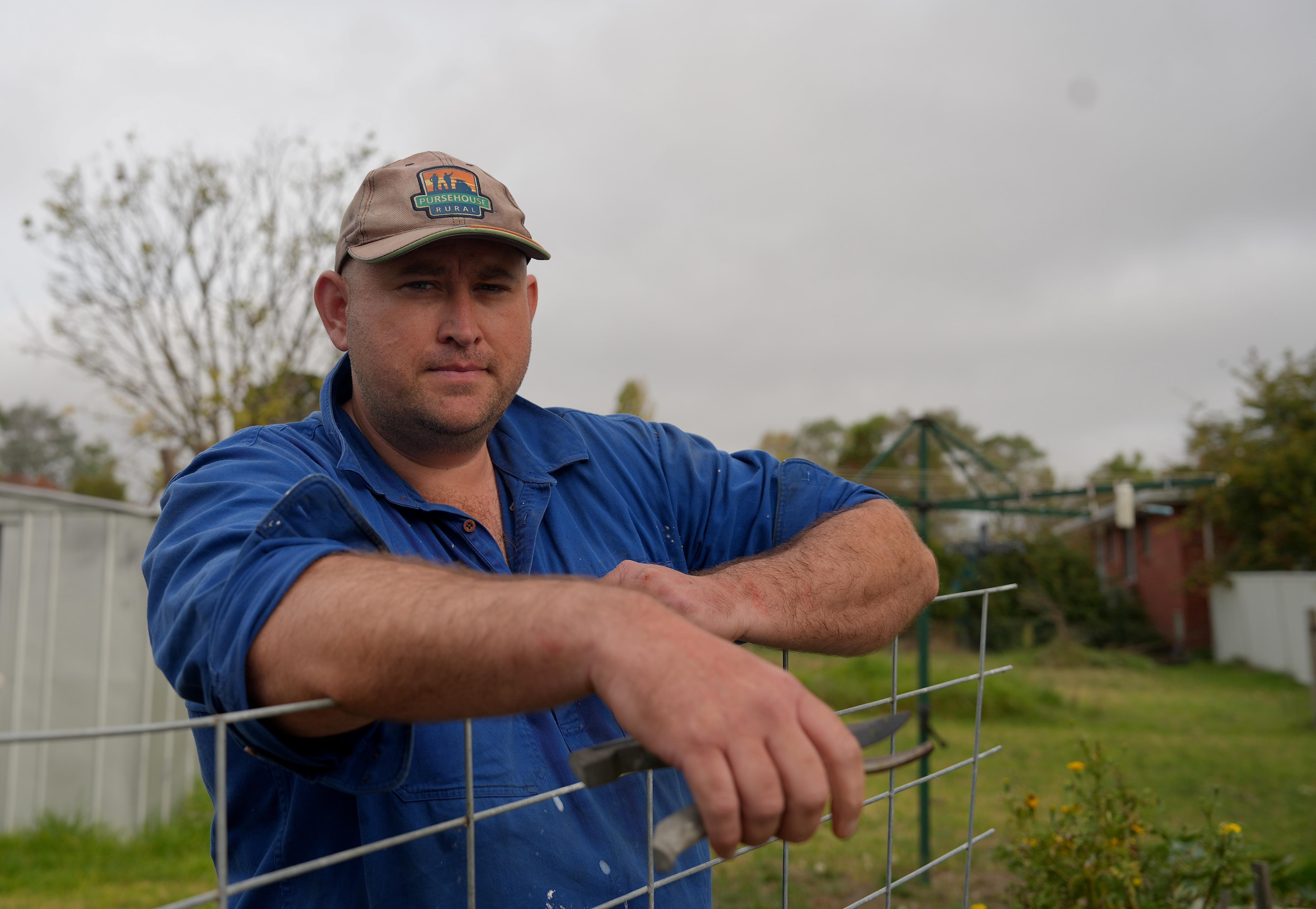 A man leans against a wire fence.