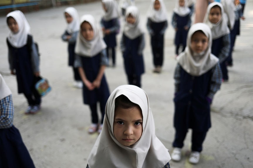 阿富汗女学生站在外面，穿着制服和头巾。
