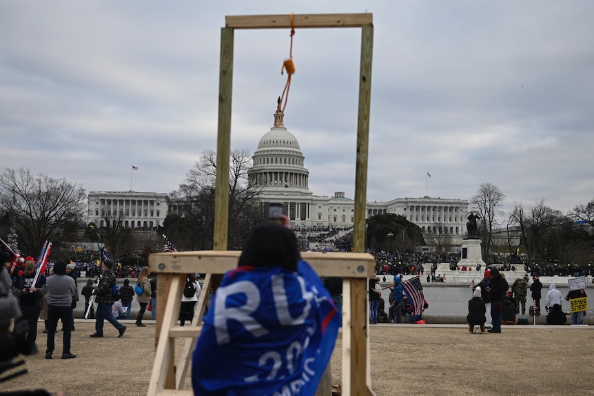 A person draped in a Trump flag stands in front of a noose erected outside the US Capitol.