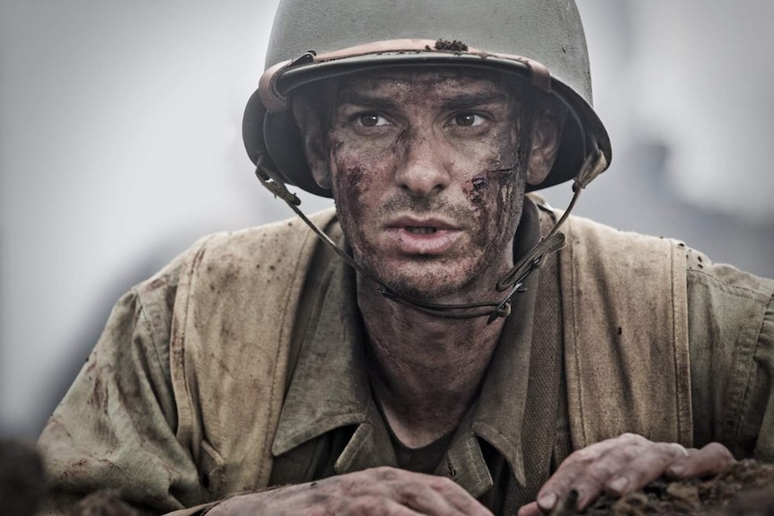 The mud-covered face of Andrew Garfield looks out from a trench in a scene from Hacksaw Ridge.