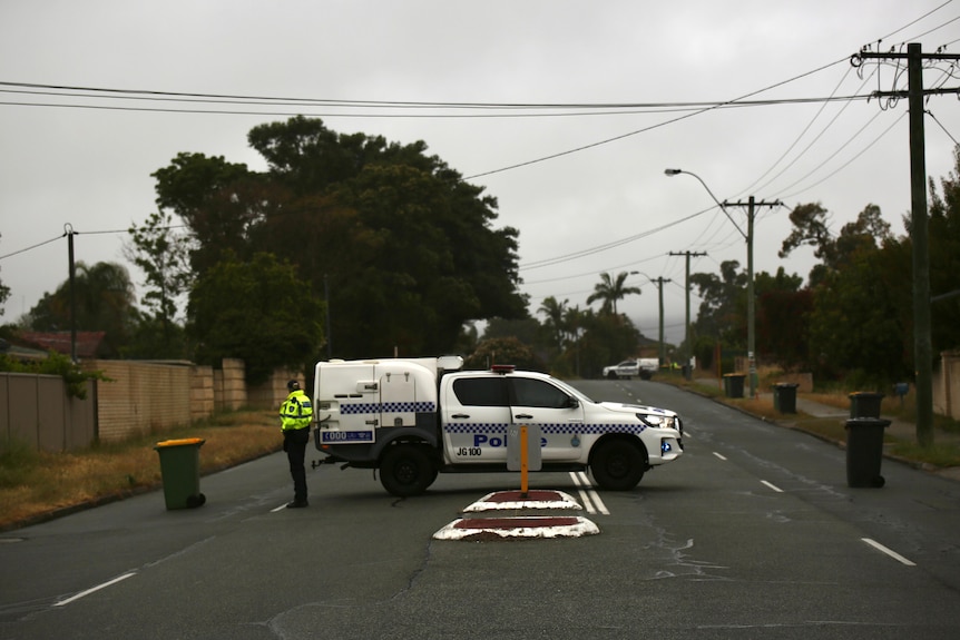 A wide shot of a residential street in Perth witha  police utility and an officer stationed in the middle of the road.