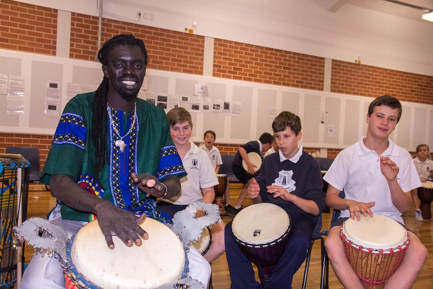 Senegalese drummer, Yacou Mbaye, sits at a West African drum with three boys from Bathurst Public behind him