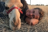 A man and camel lie on the ground looking at the camera.